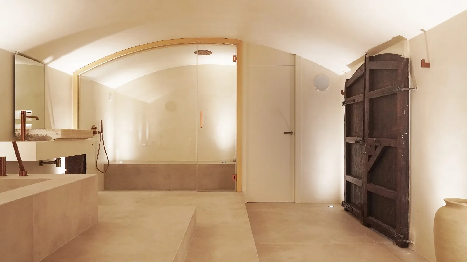 Baño de vapor de microcemento con puerta acristalada en arco y banco corrido, en Teià