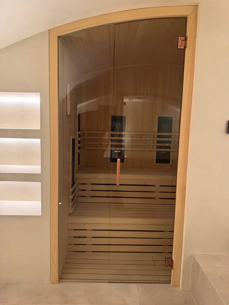 Cabina de infrarrojos de techo abovedado, con los emisores en la pared del fondo vistos a través de la doble puerta de cristal.