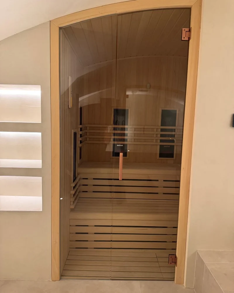 Cabina de infrarrojos de techo abovedado, con los emisores en la pared del fondo vistos a través de la doble puerta de cristal.