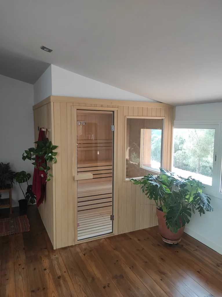 Sauna de interior encajada bajo una cubierta inclinada, rematada a la altura del alero y con una ventana interior que da al pinar.