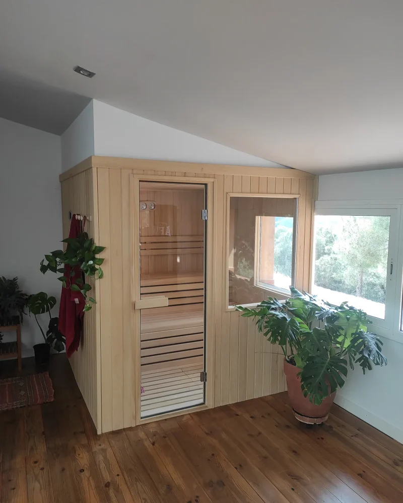 Sauna de interior encajada bajo una cubierta inclinada, rematada a la altura del alero y con una ventana interior que da al pinar.