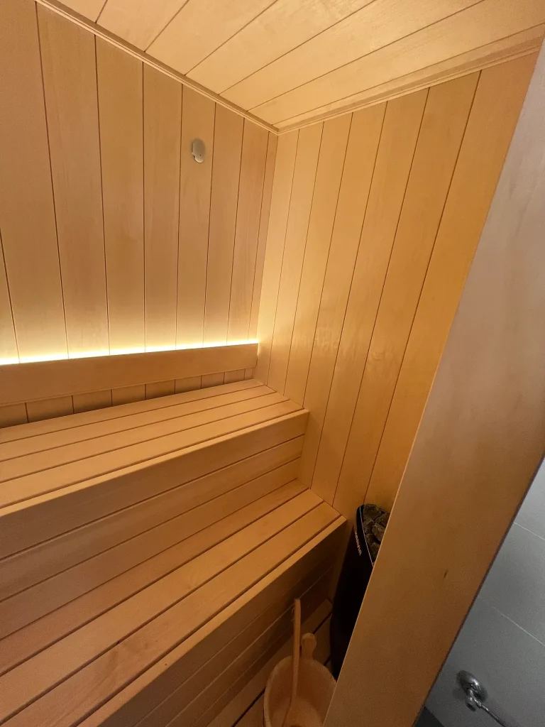 Interior de una sauna pequeña con dos alturas de banco y una tira de luz cálida escondida bajo el respaldo.