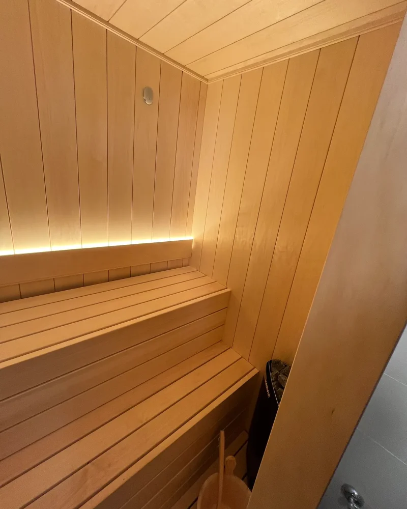 Interior de una sauna pequeña con dos alturas de banco y una tira de luz cálida escondida bajo el respaldo.
