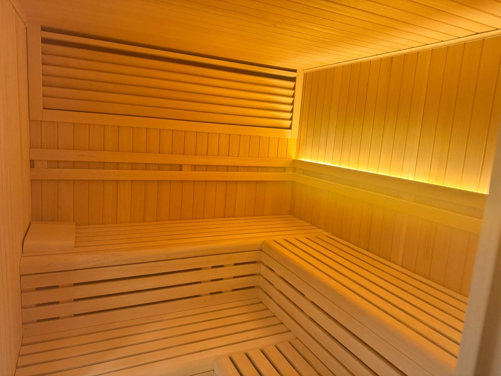 Sauna de interior con los bancos dispuestos en L y una luz indirecta que recorre todo el respaldo.