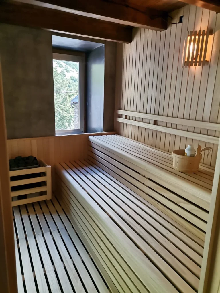 Sauna con bancos de dos alturas, estufa de piedras y una ventana que da a los tejados y la ladera del valle.