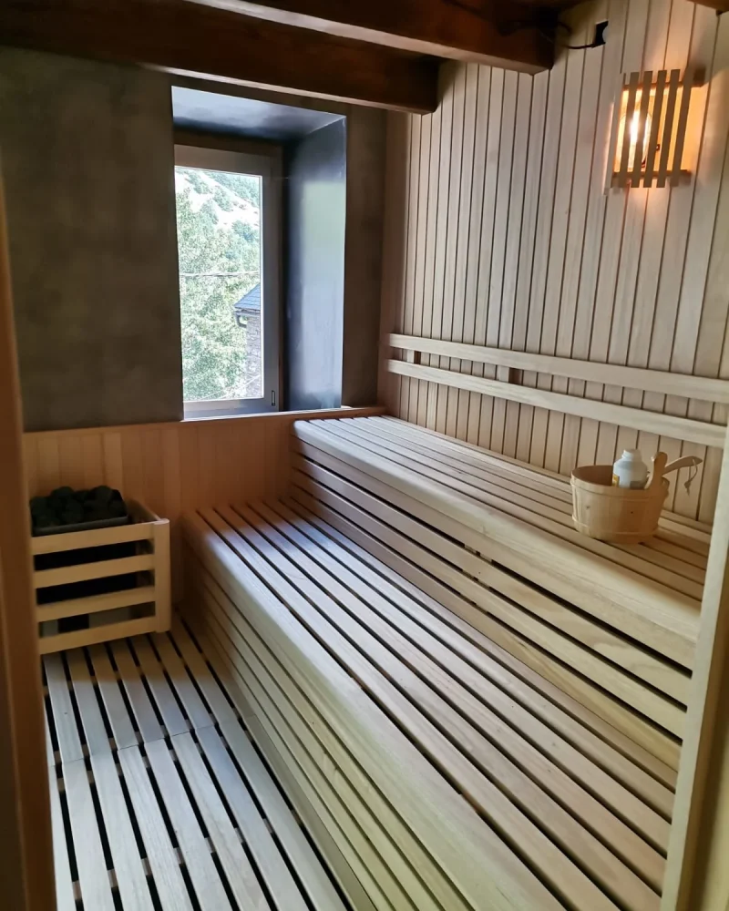 Sauna con bancos de dos alturas, estufa de piedras y una ventana que da a los tejados y la ladera del valle.